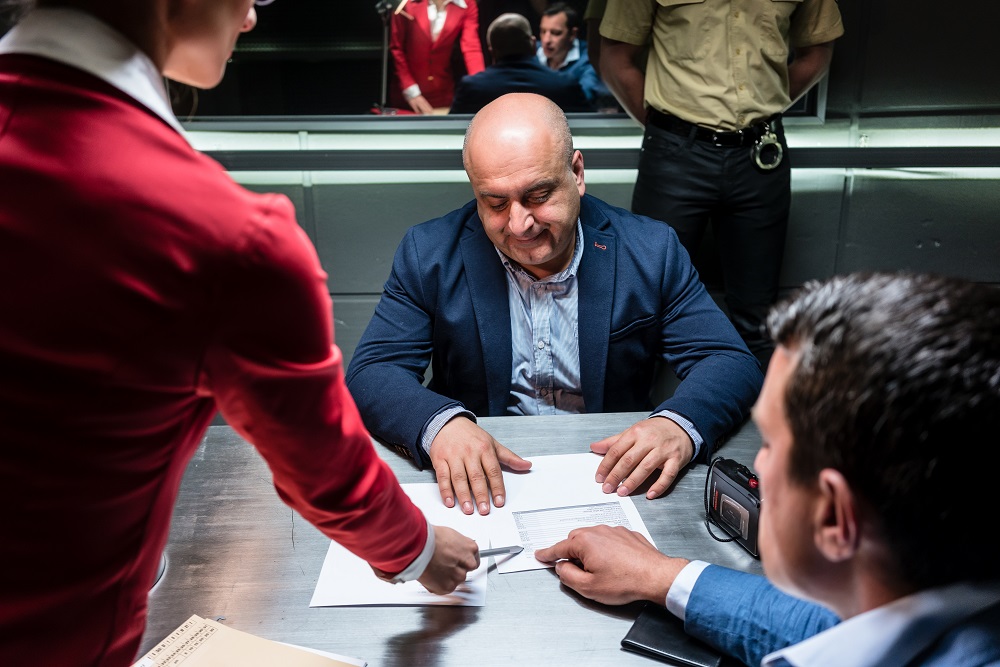 Middle-aged defendant or witness, counseled by the lawyer to sign an official statement in front of the prosecutor during a criminal investigation in the police station.