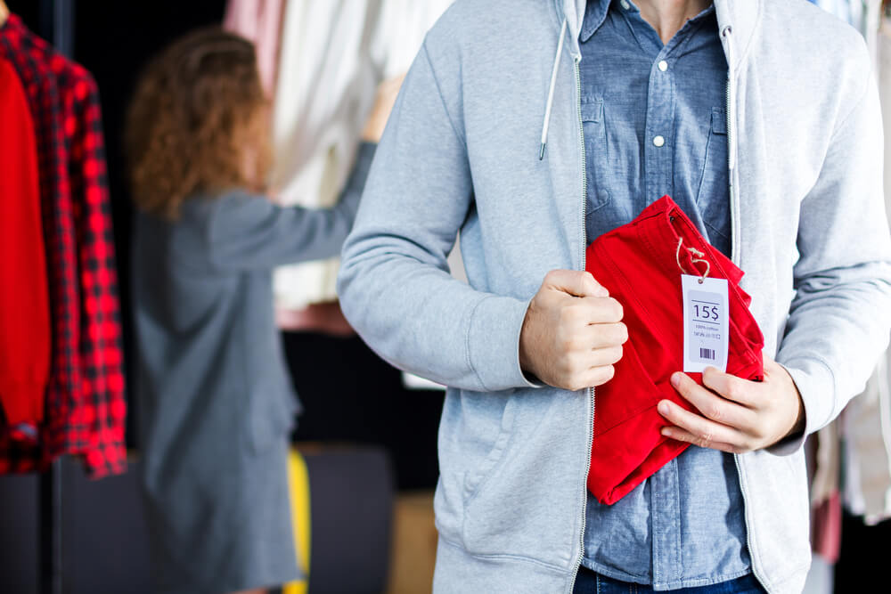 Young man is stealing red jeans in store, shop, boutique at shopping center.