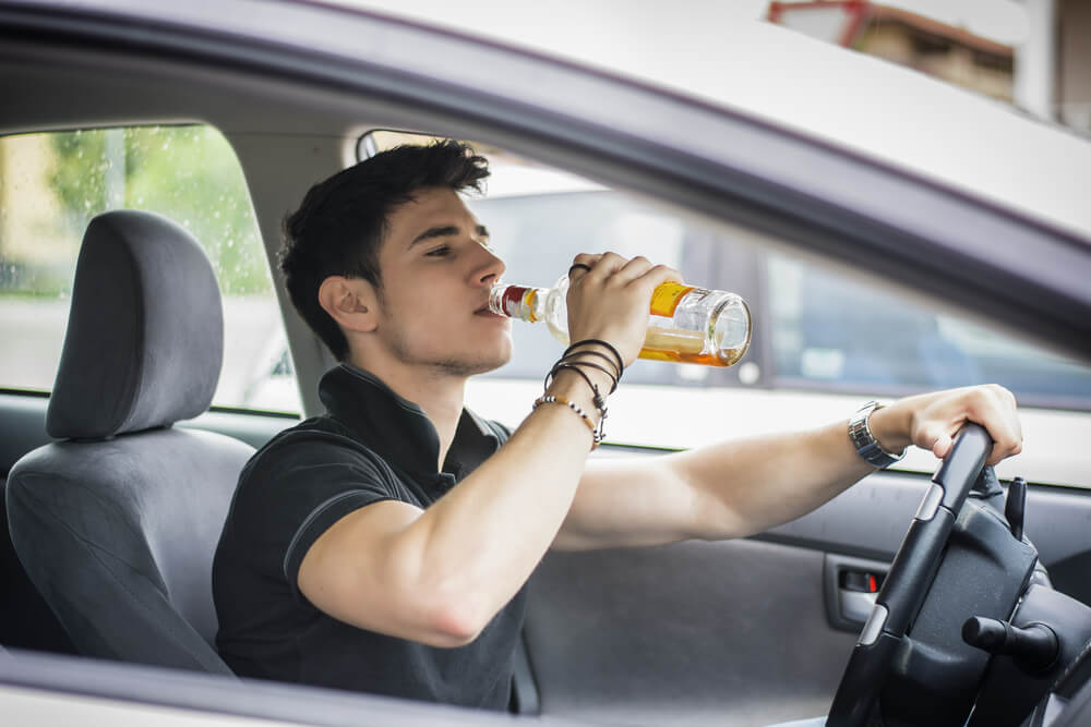 Young man driving his car while drinking alcohol in the traffic.