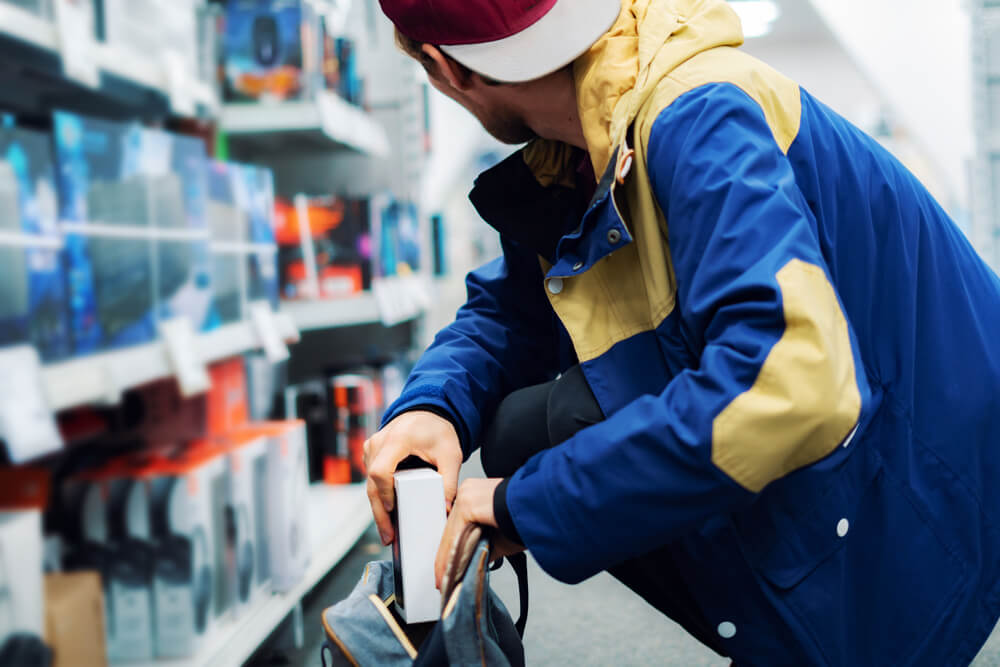 Shoplifter in the electronic store supermarket stealing new gadget.